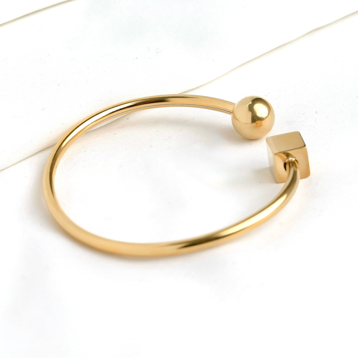 Close-up view of gold cue and ball cuff bracelet with spherical and square ends on a white background