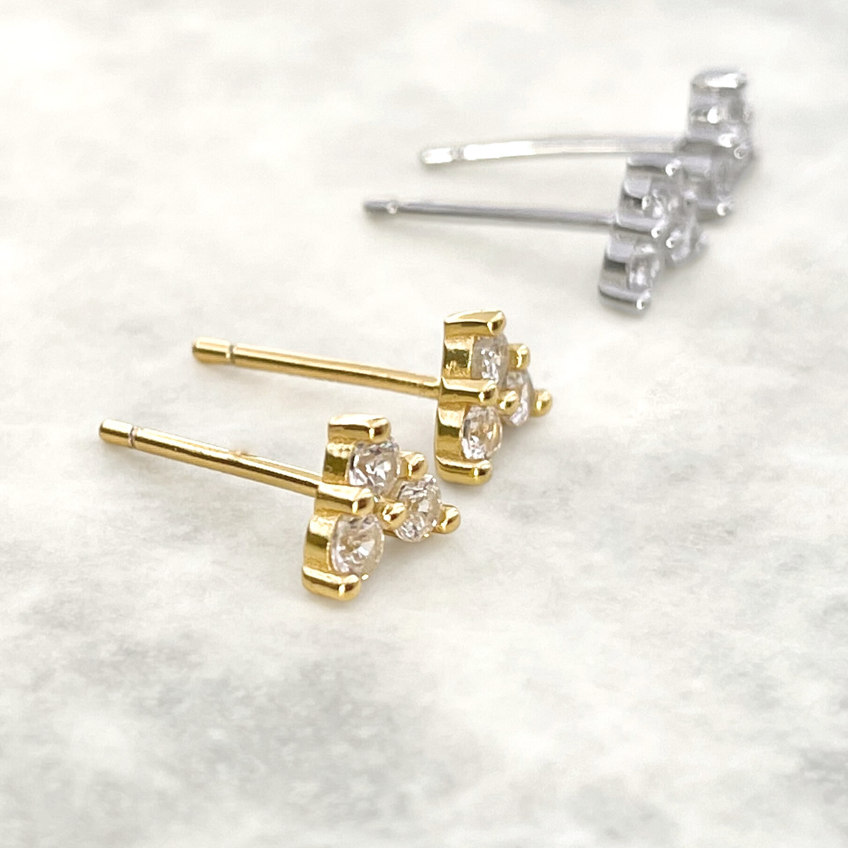 Gold and silver CZ clover stud earrings on a light gray background