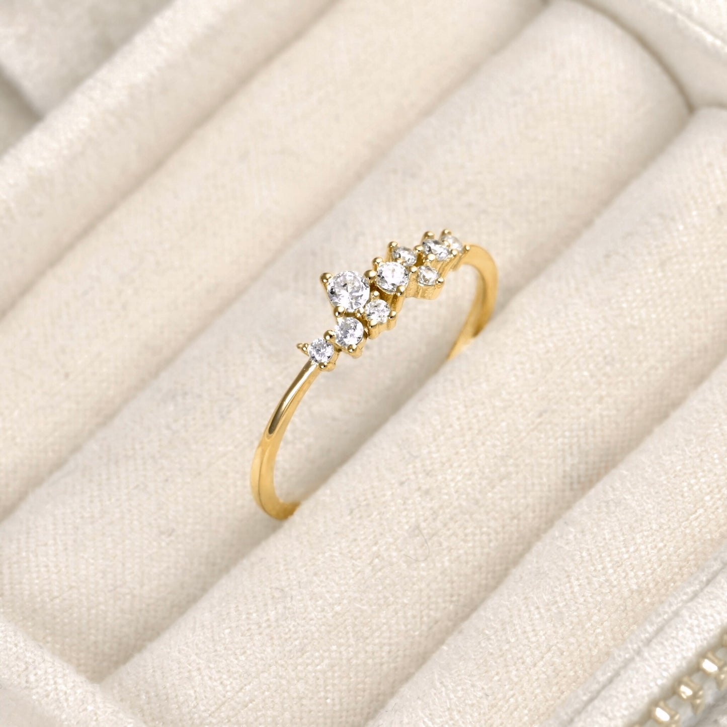 A yellow gold ring with a cluster of clear round-cut gemstones, displayed on a cream-colored velvet jewelry box.