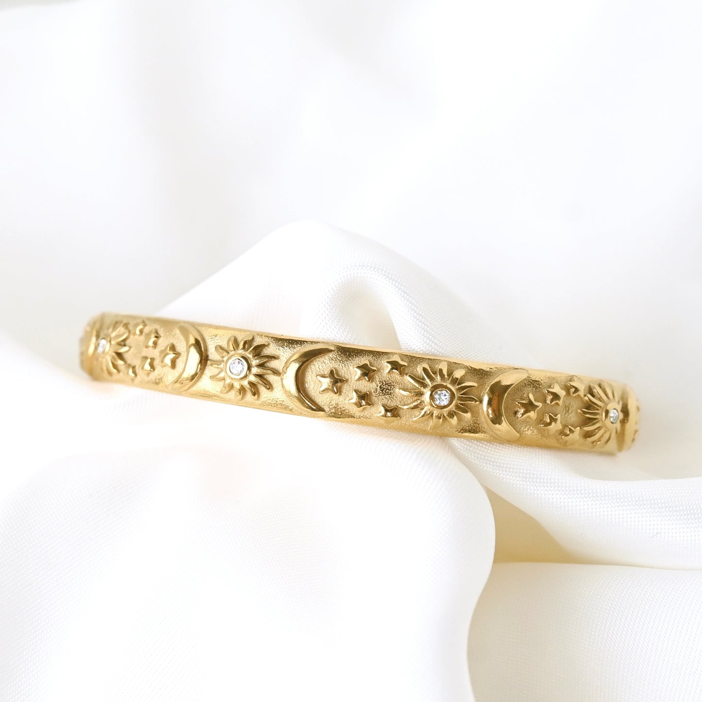 Gold open bangle with decorative sun, moon and stars on a white fabric background