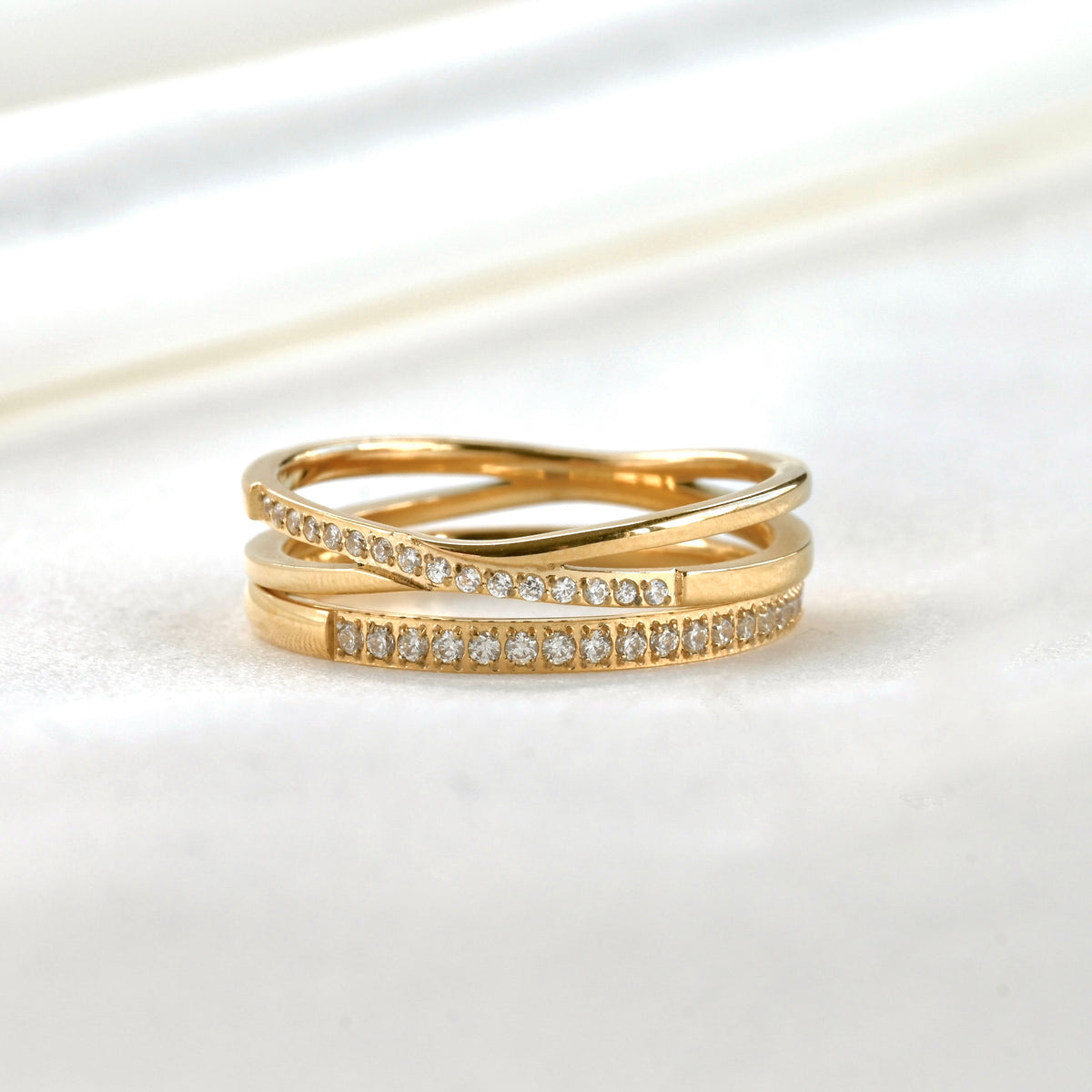 Two gold rings with diamond accents stacked, slim ring on bottom and X ring on top, on a white background
