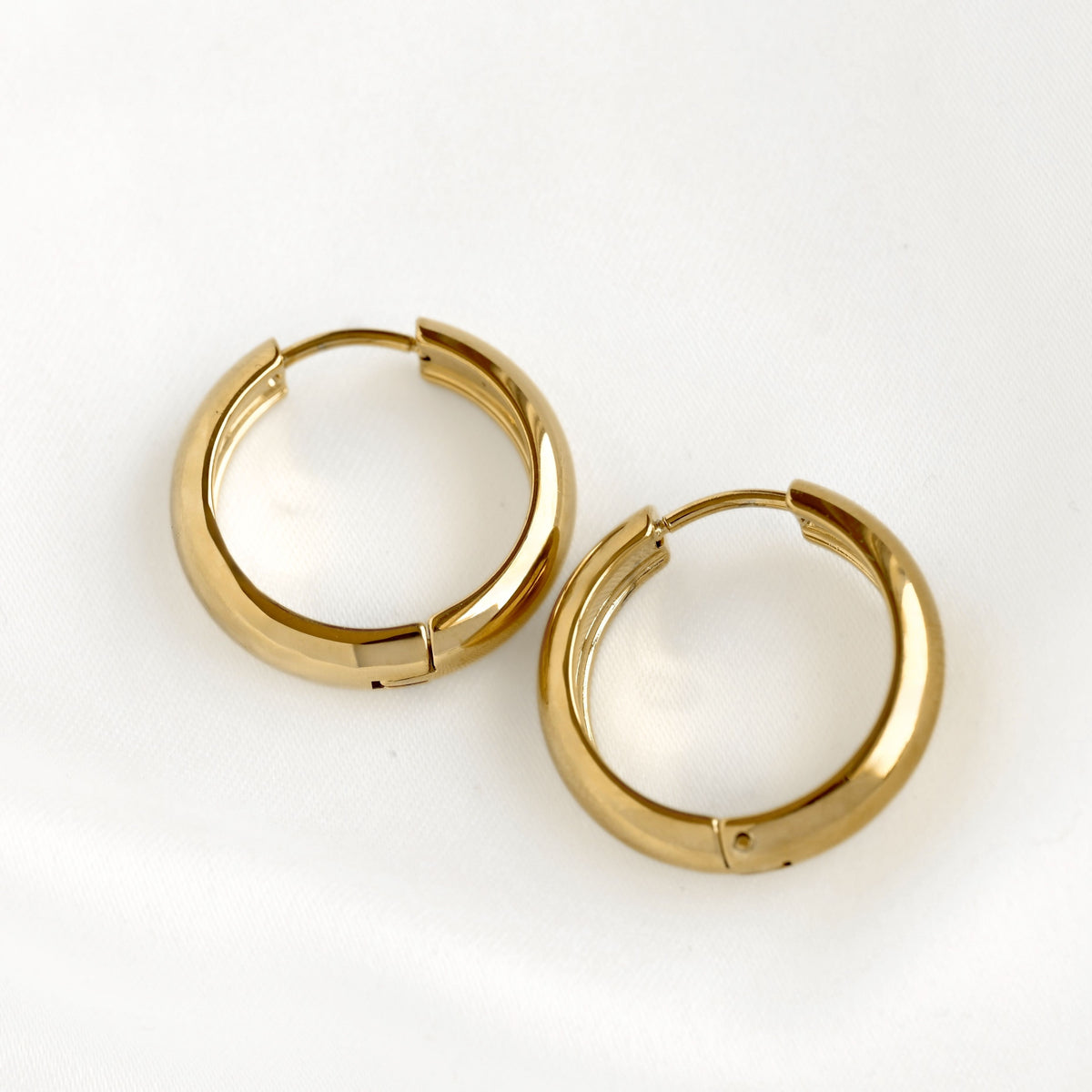 A pair of polished 21 mm gold huggie hoop earrings on a clean white background.