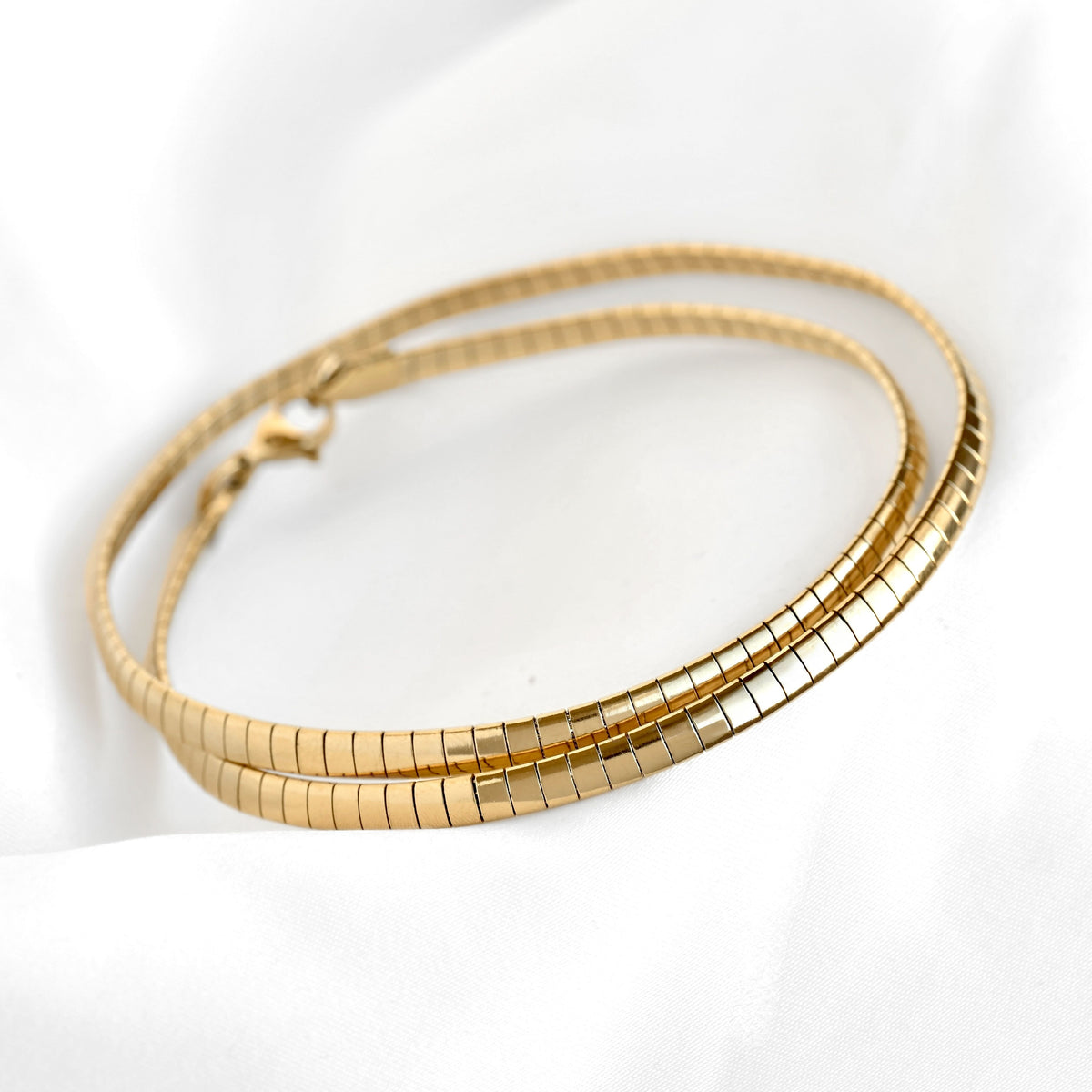 A gold-toned omega chain necklace with a lobster clasp, resting on a white fabric background.