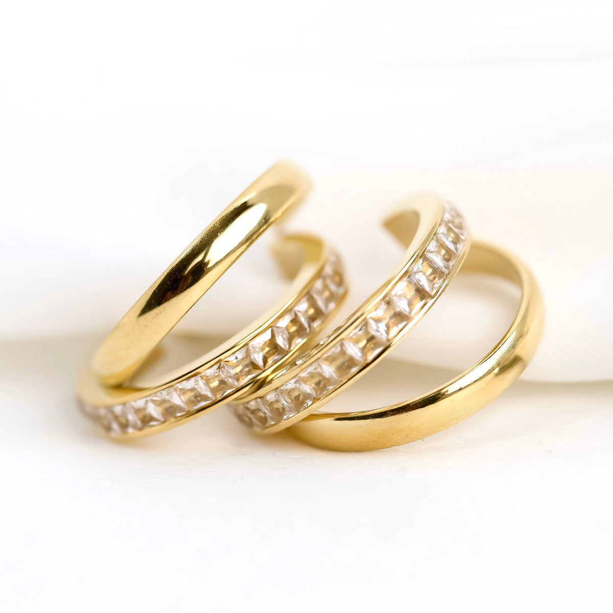Two gold hoop earrings with channel set crystals on a white background
