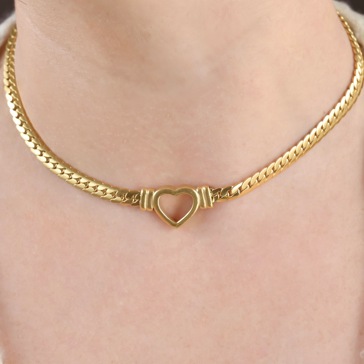 Statement heart necklace in gold on a person's neck.