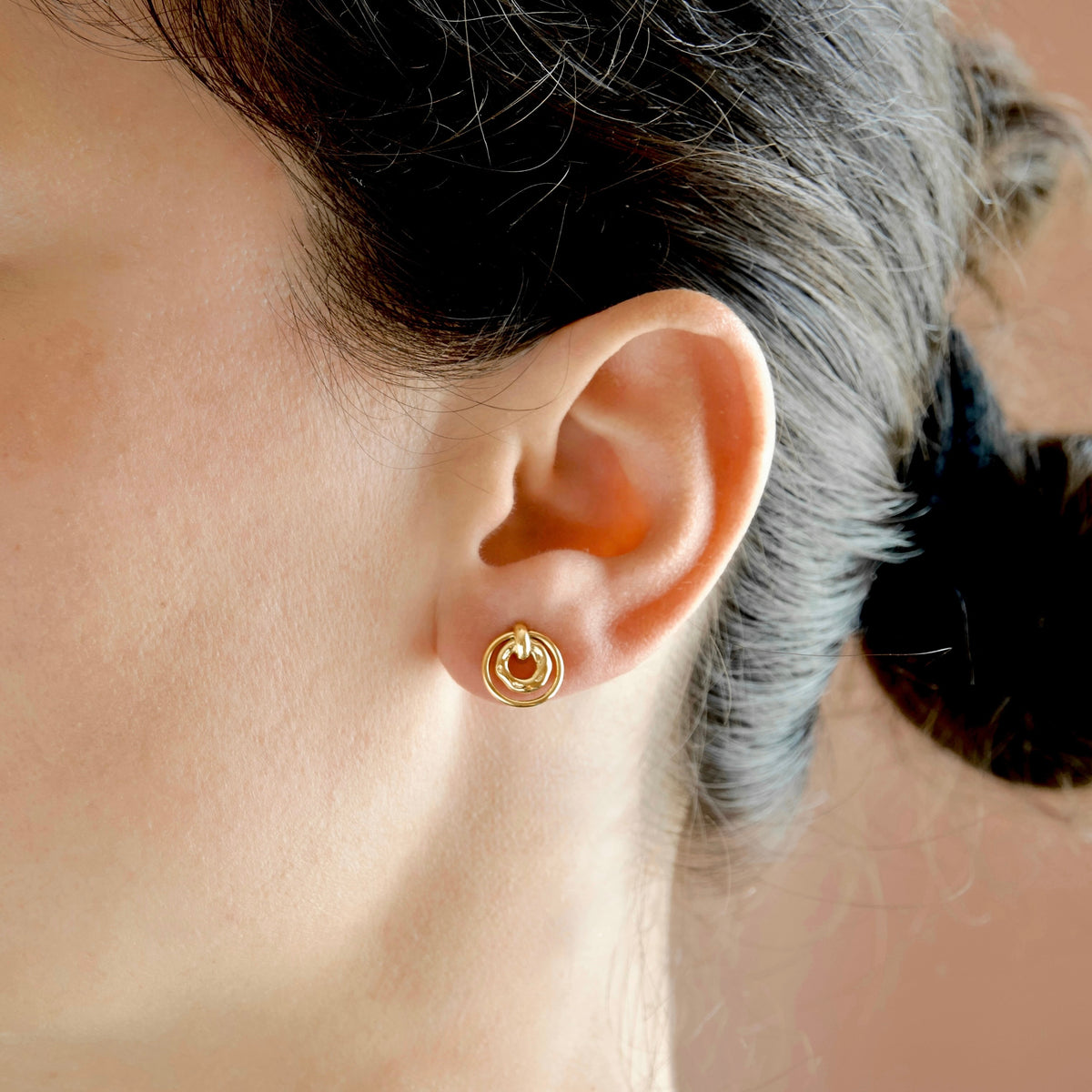 A close-up of a person's ear wearing a small gold hoop earring with a circular inner detail.