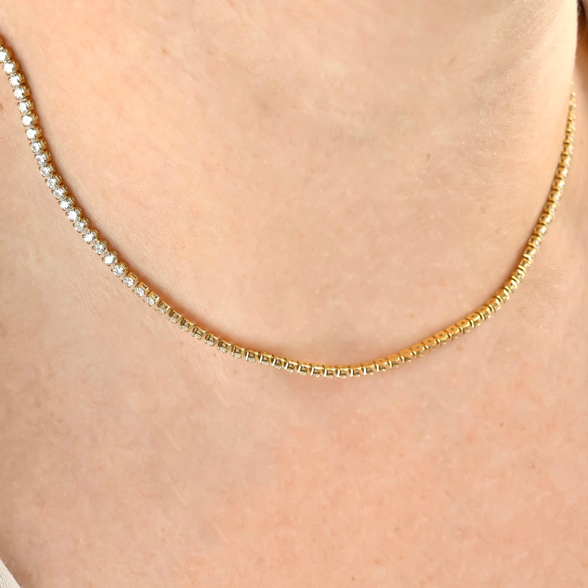 Gold stone and cup chain necklace on a person's neck against a neutral background