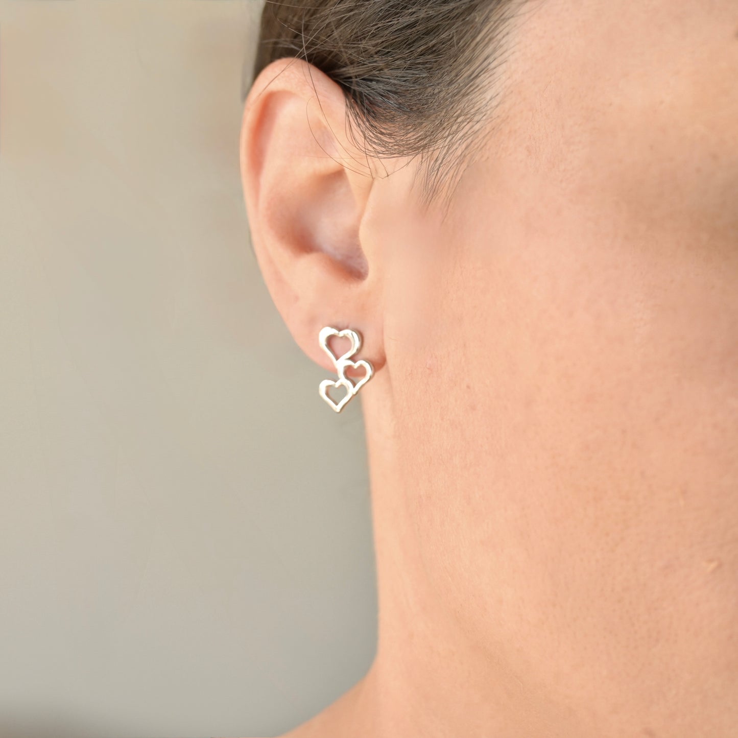 Close-up of a person wearing silver heart-shaped earrings against a neutral background