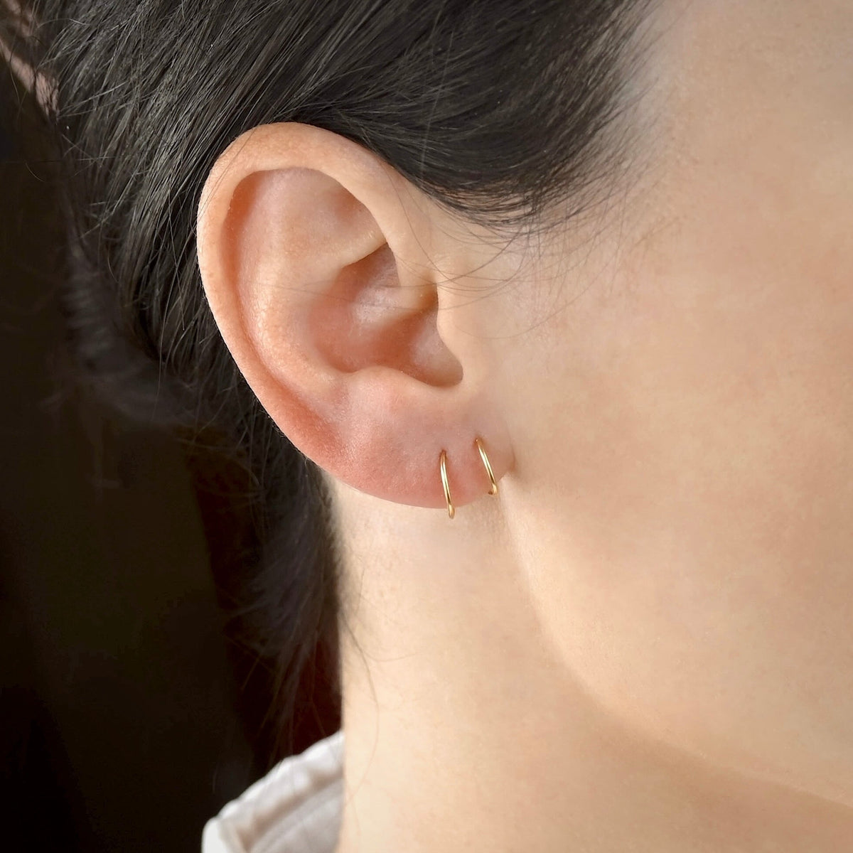 Close-up of an ear wearing a tiny twist-in gold hoop earring with a blurred background