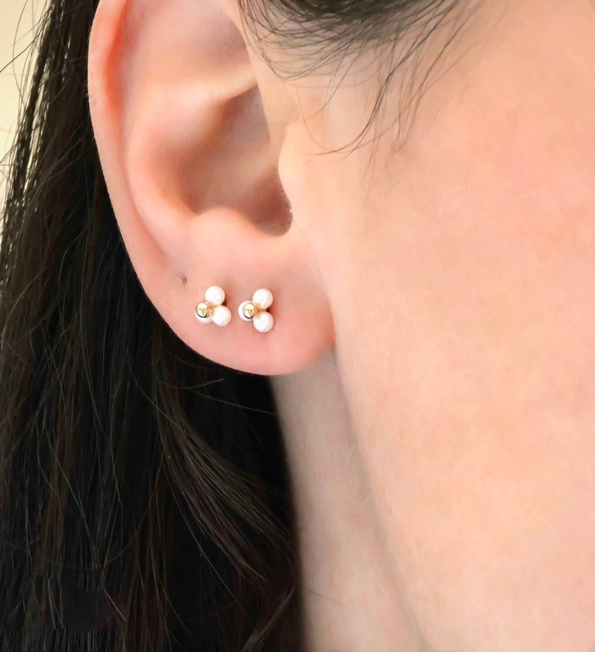 Close-up of an ear wearing two triplepearl cluster earrings with rose gold posts.