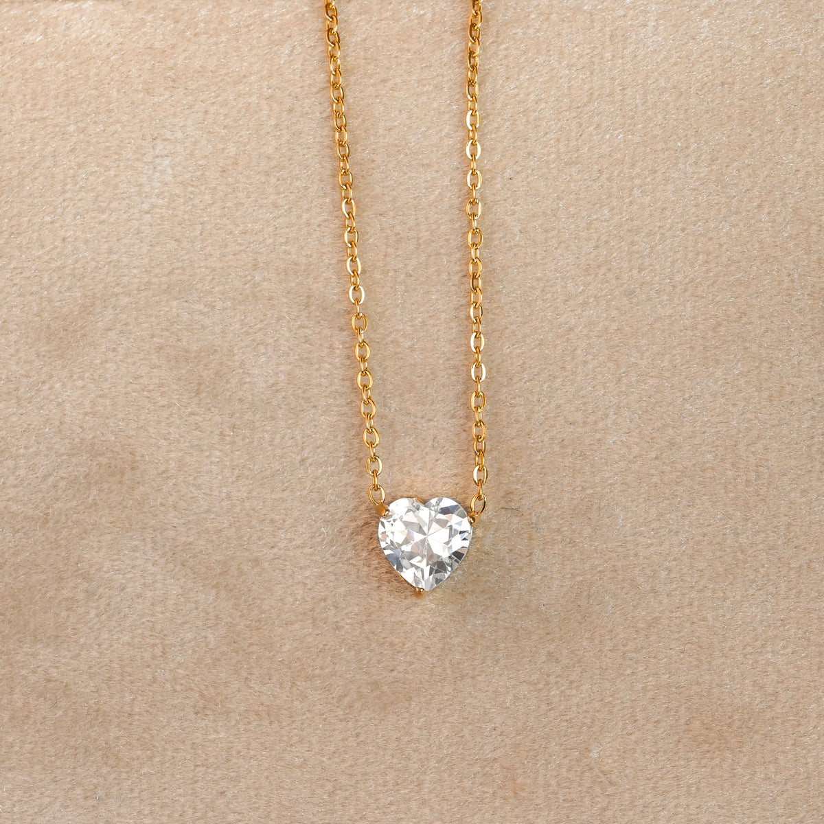 Heart-shaped diamond pendant on a gold chain against a beige background