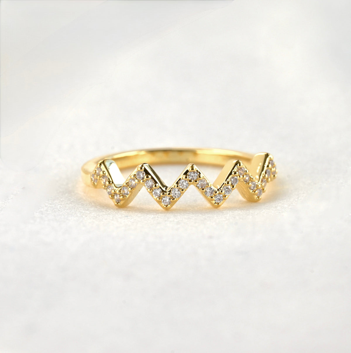 Pave CZ zig zag ring in gold on a white surface.