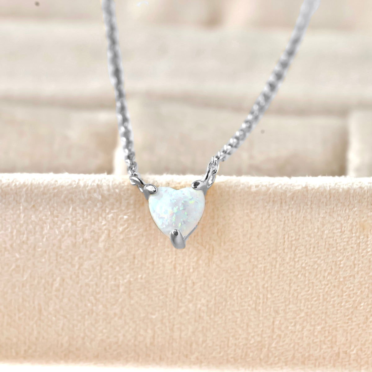 Silver necklace with a heart-shaped opal pendant on a beige background