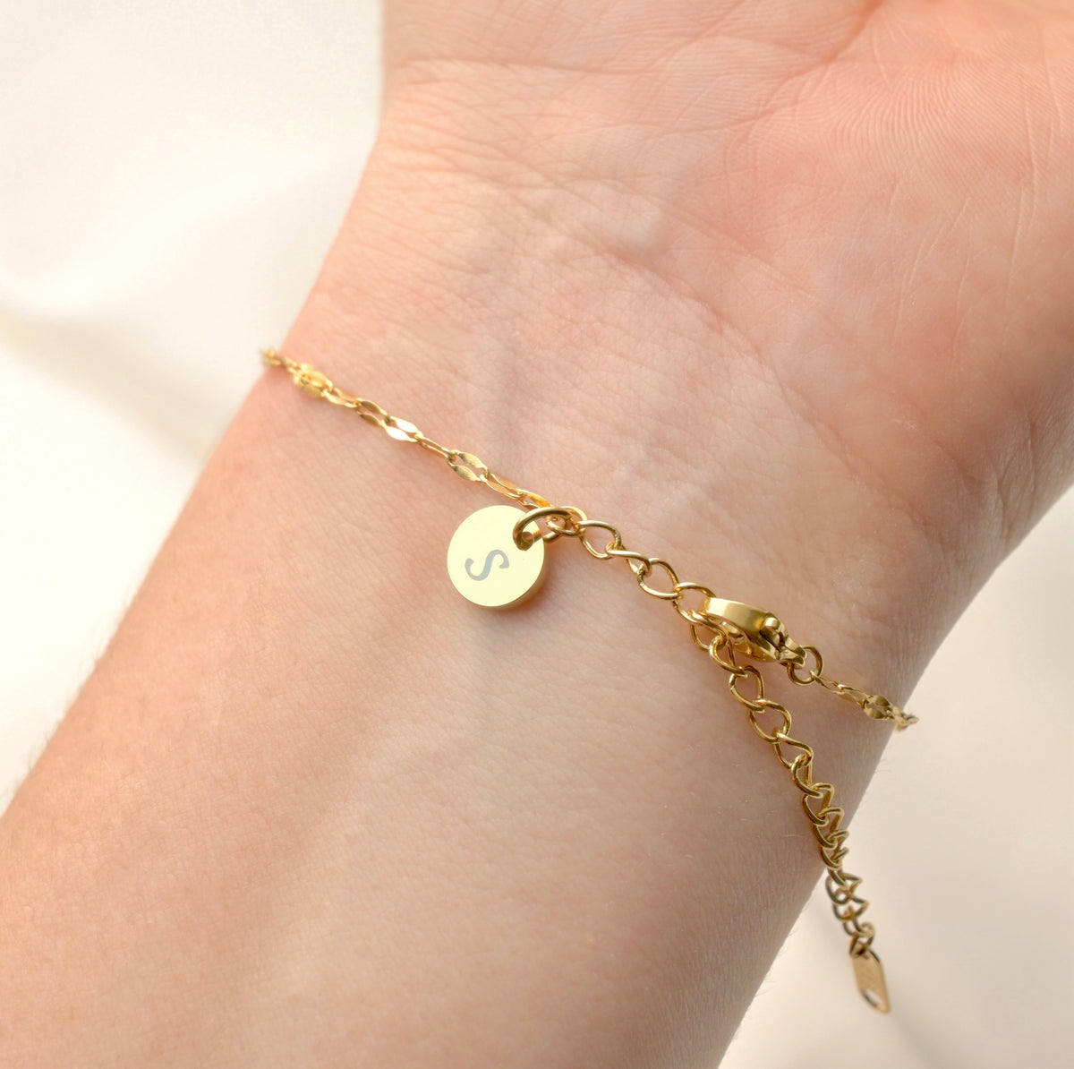 Dainty gold mariner bracelet with a round initial charm on a wrist against a neutral background
