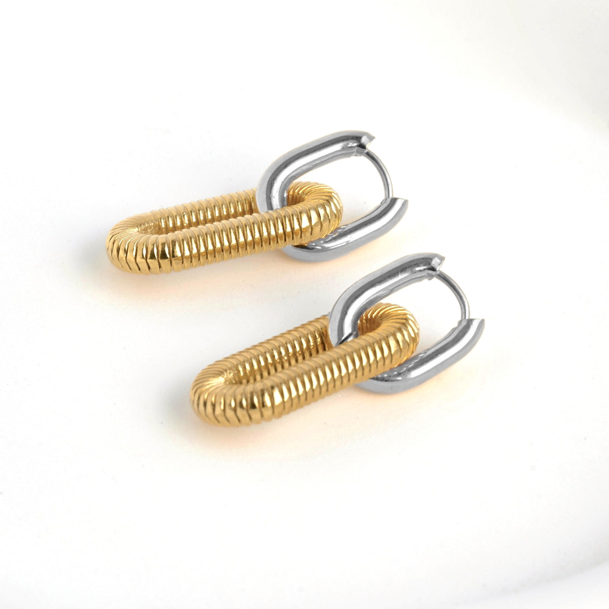 Pair of two tone earrings with silver U shaped hoop with clicker closure and an attached gold textured link on a white background
