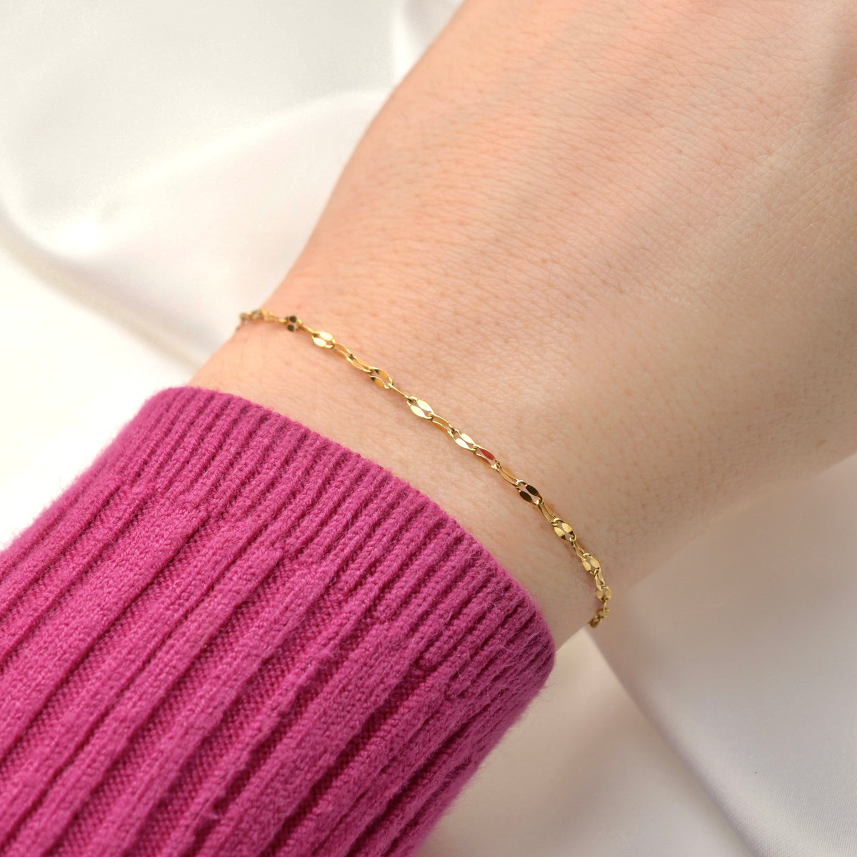 Gold bracelet on a wrist with a pink sleeve against a white background