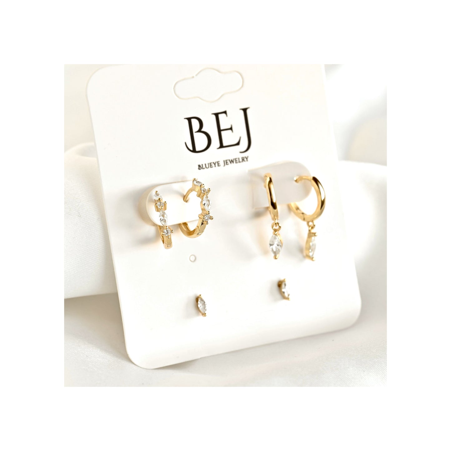 A pair of gold huggie hoop earrings with clear crystal accents and matching small stud earrings, displayed on a white card labeled BEJ Marine Jewelry.