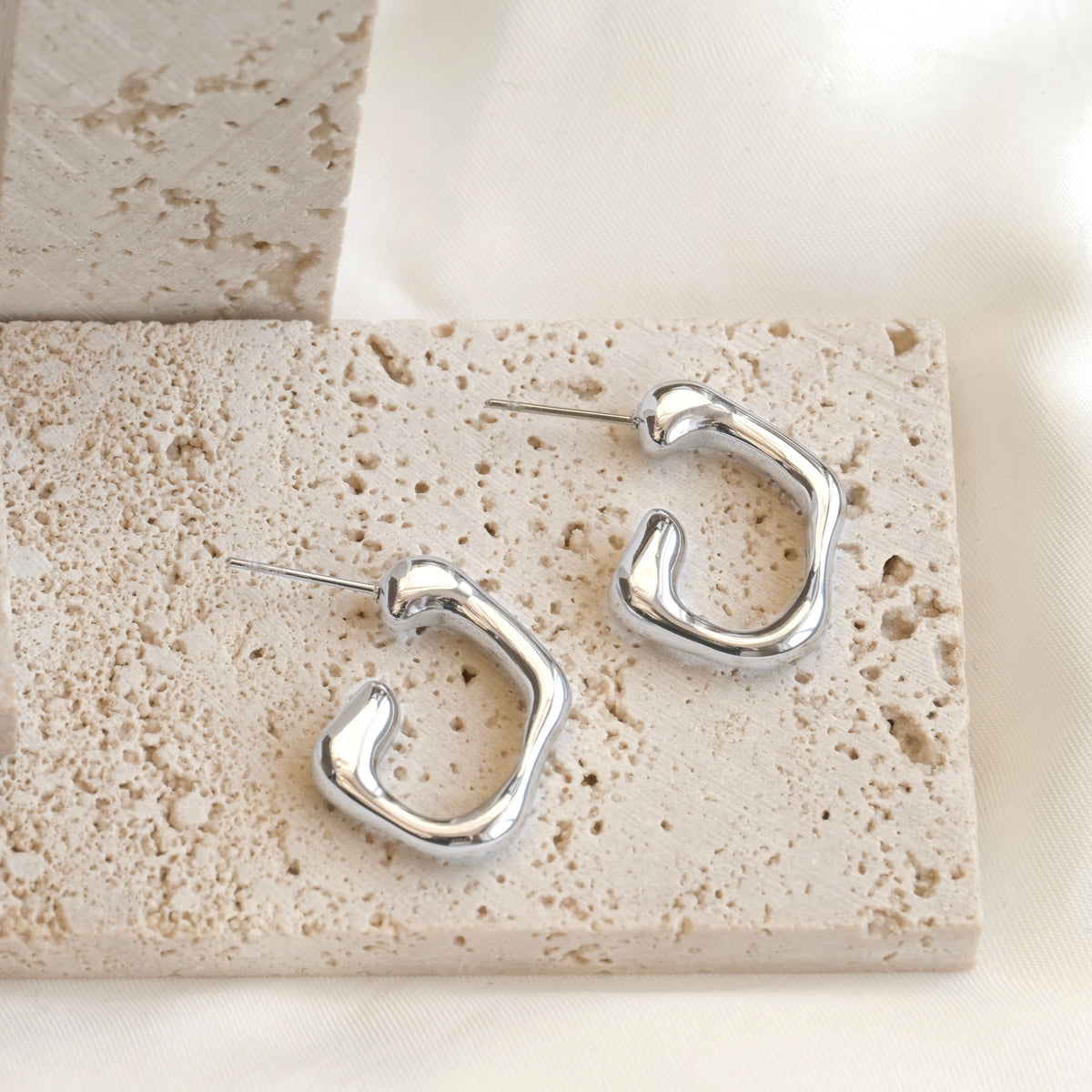 Silver molten hoop earrings on a textured stone surface