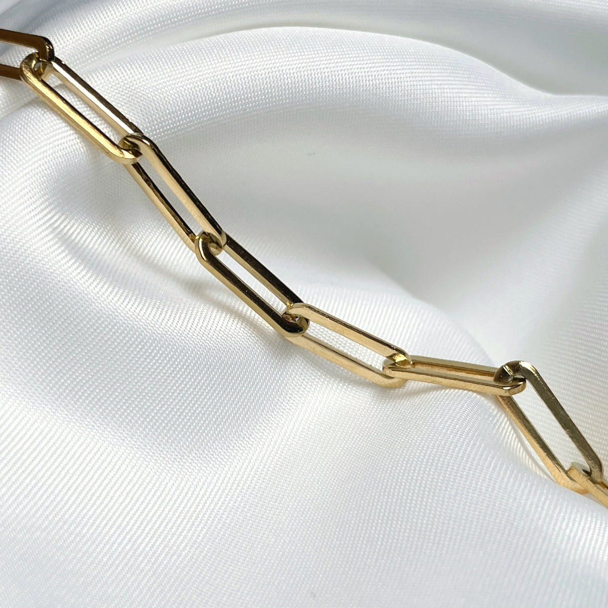 Close-up view of chunky gold paperclip links on a white fabric background
