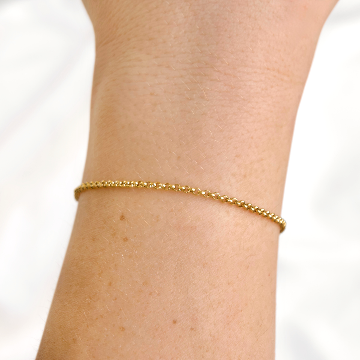 Gold rolo chain bracelet on a wrist against a white background