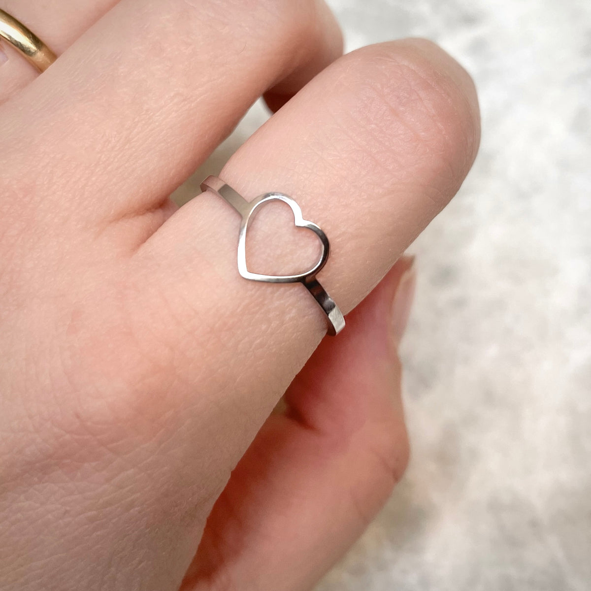 Silver heart ring on index finger with a blurred background