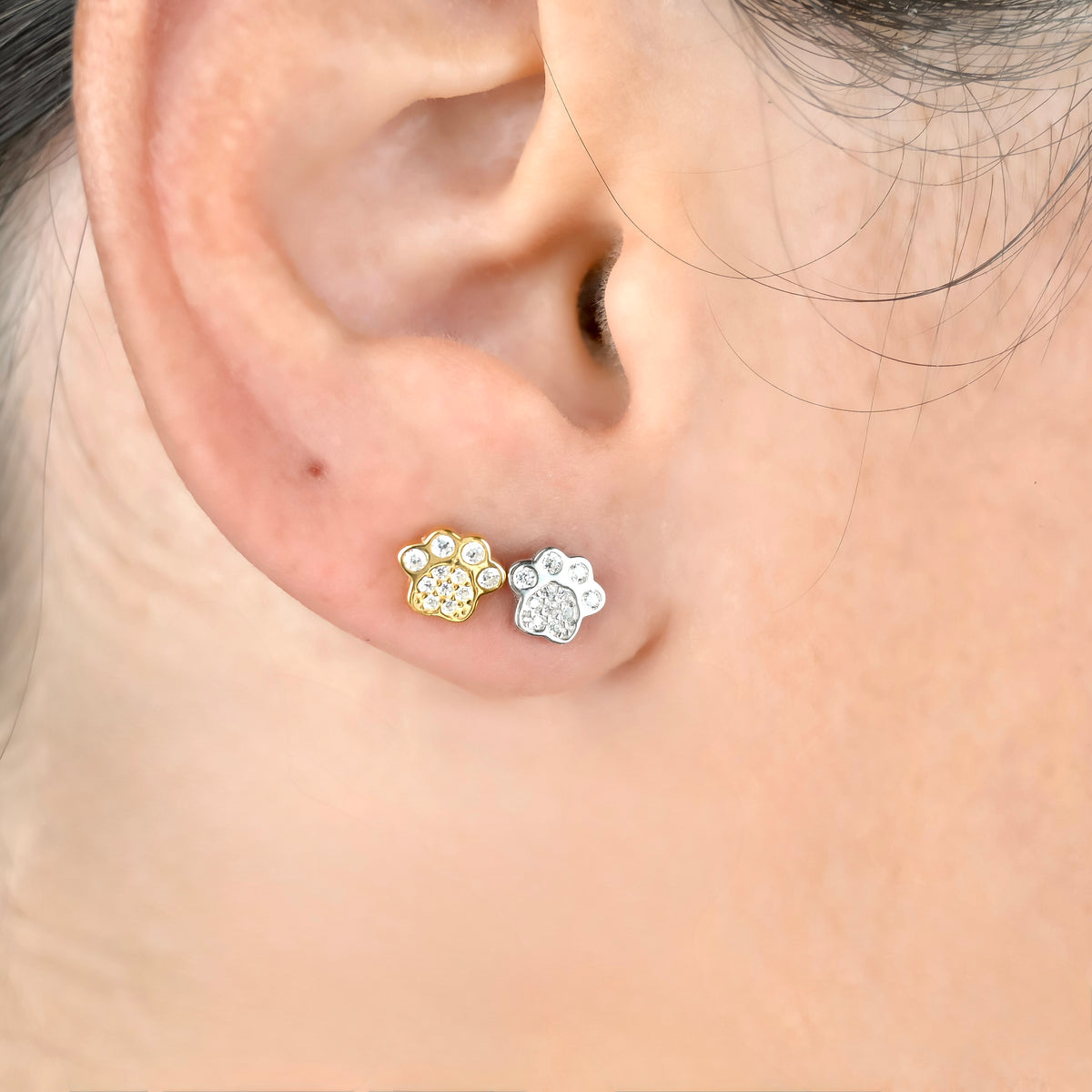 Close-up of an ear wearing gold and silver paw print earrings pave-set with clear CZ