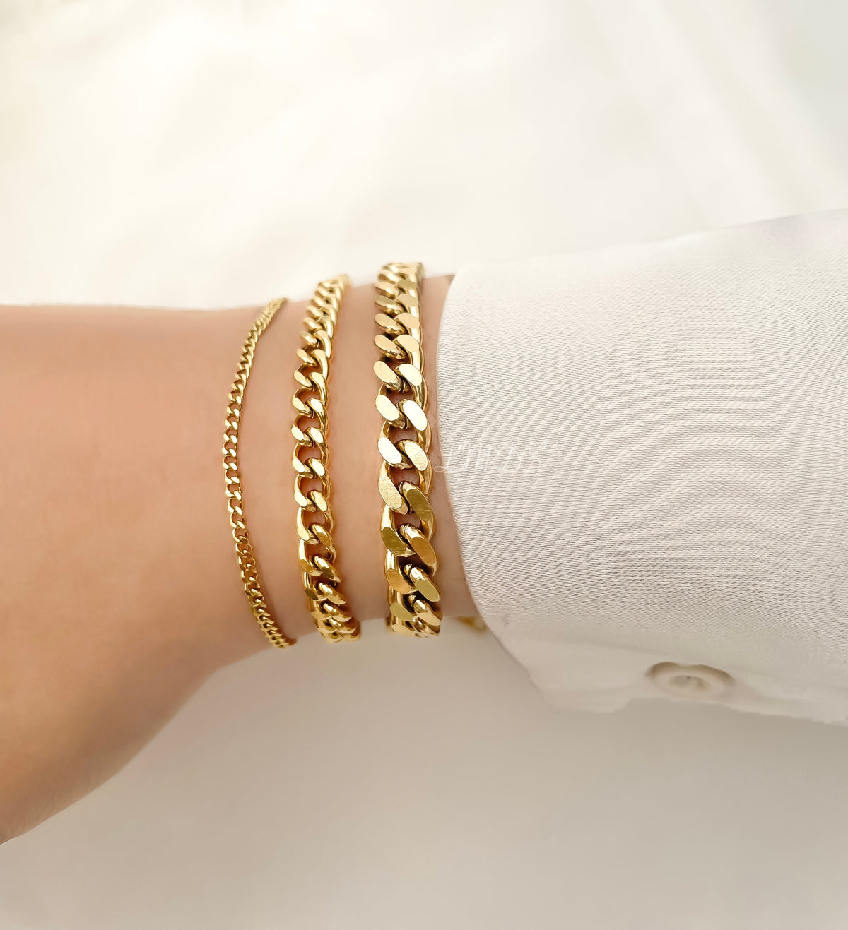 Gold curb chain bracelet stack on a wrist against a white background