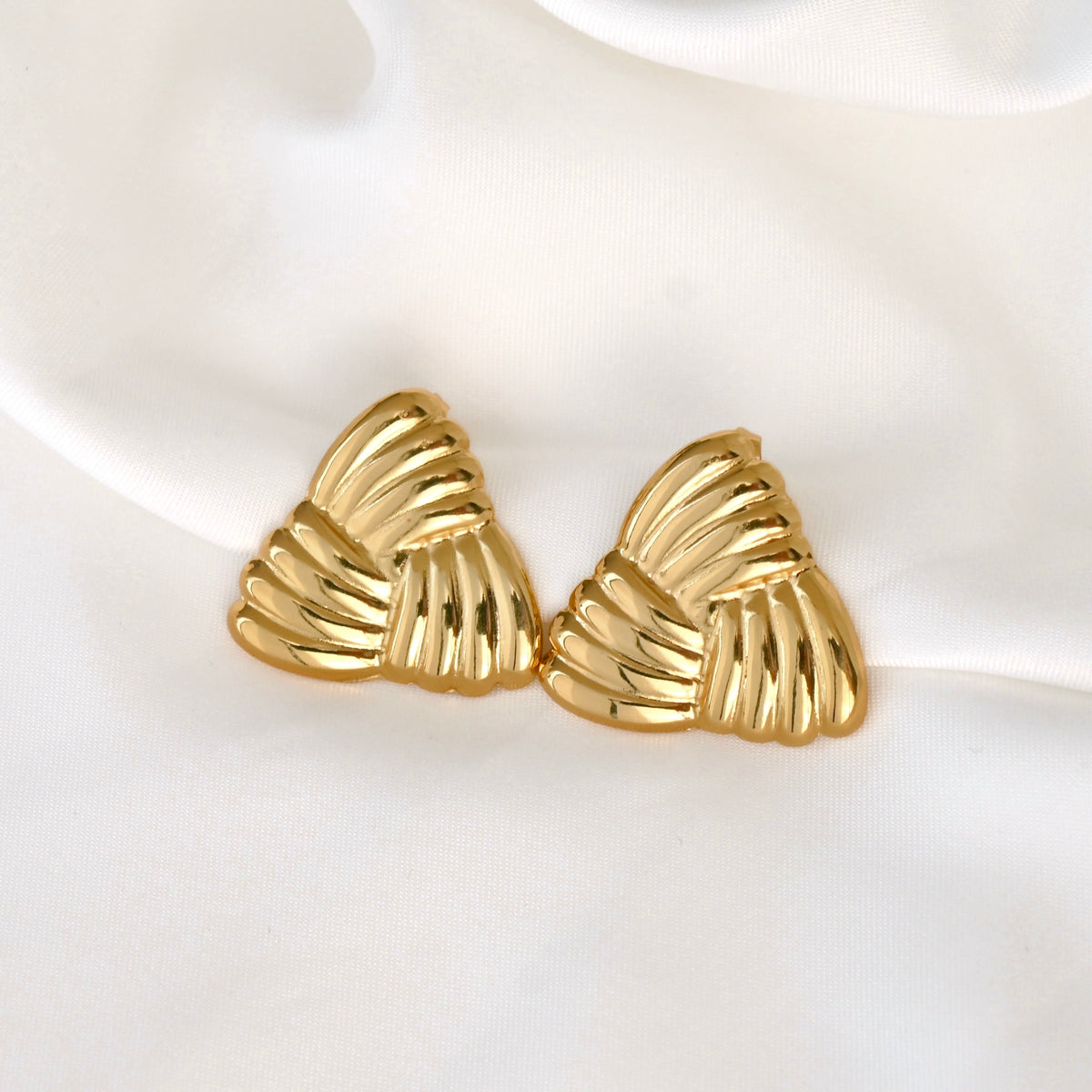 Gold triangle-shaped ribbed earrings on a white fabric
