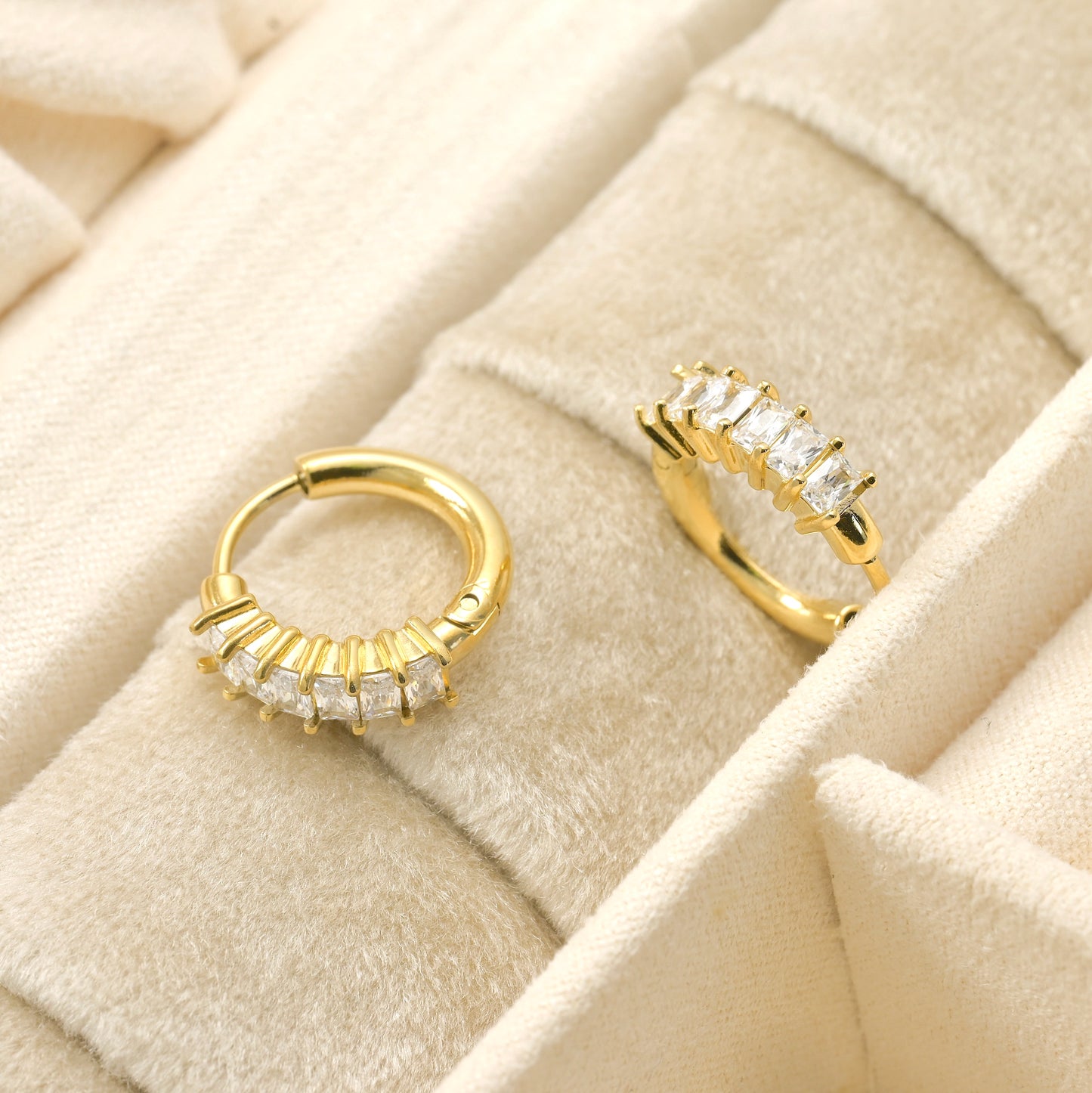 Gold hoop earrings with embedded stones on a beige textured surface