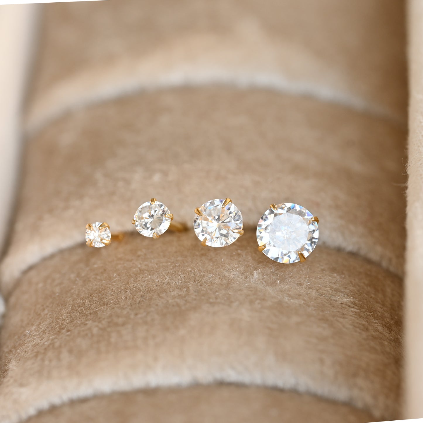 front view of four diamond stud earrings on a beige fabric background