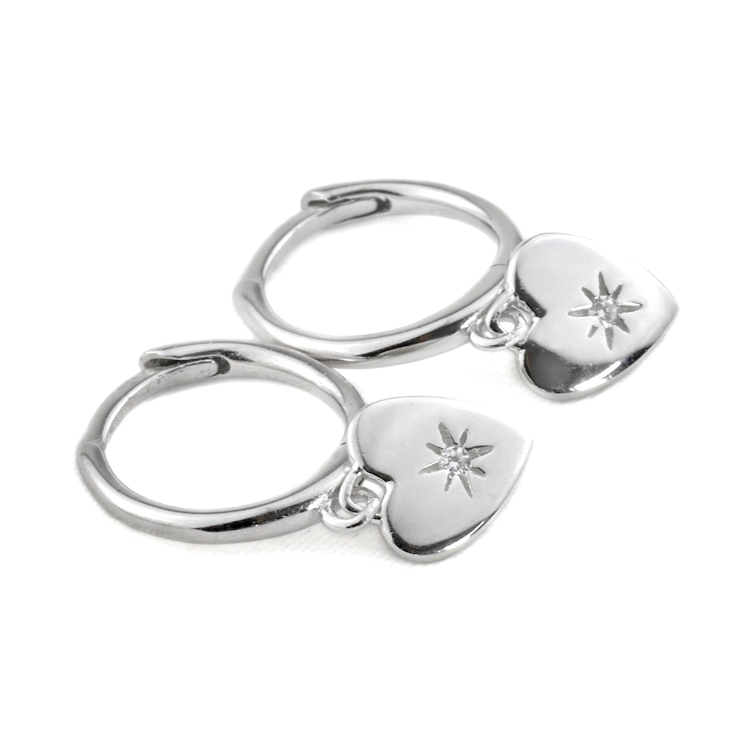 Pair of silver hoop earrings with heart-shaped charms with a star-set CZ in the center on a white background