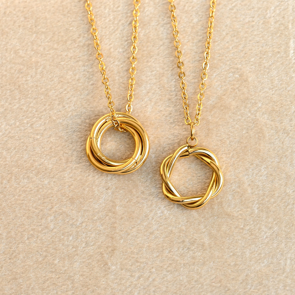 Two gold karma necklaces with interlocking ring pendants on a beige background