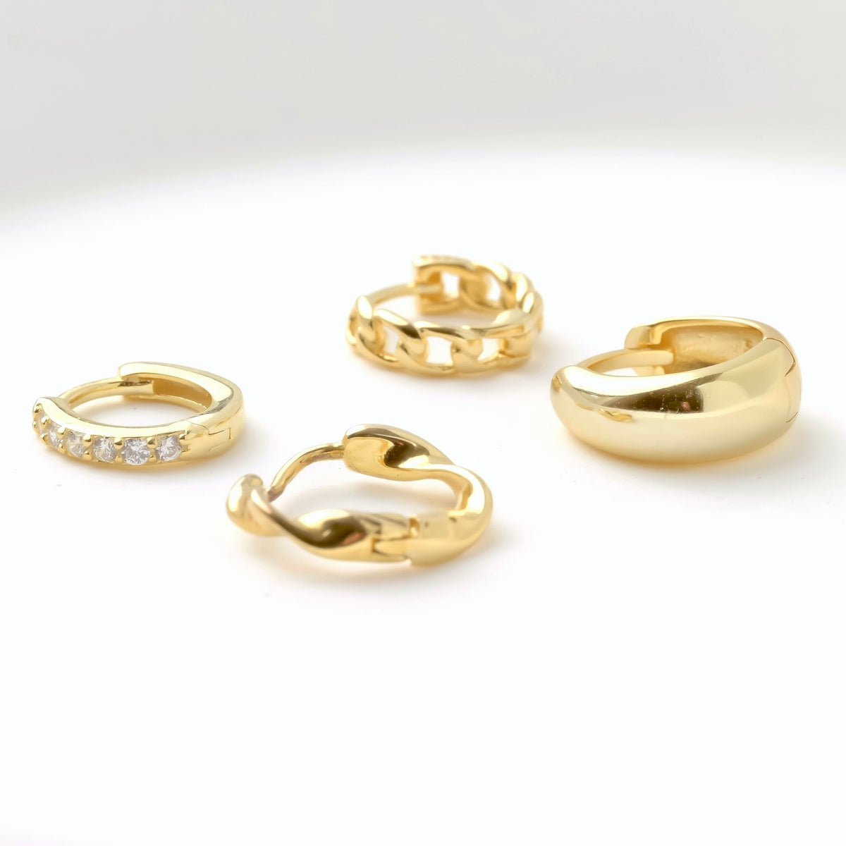 Set of mini gold hoop earrings including half eternity pave CZ, curb link chain, twisted and chunky dome on a white background