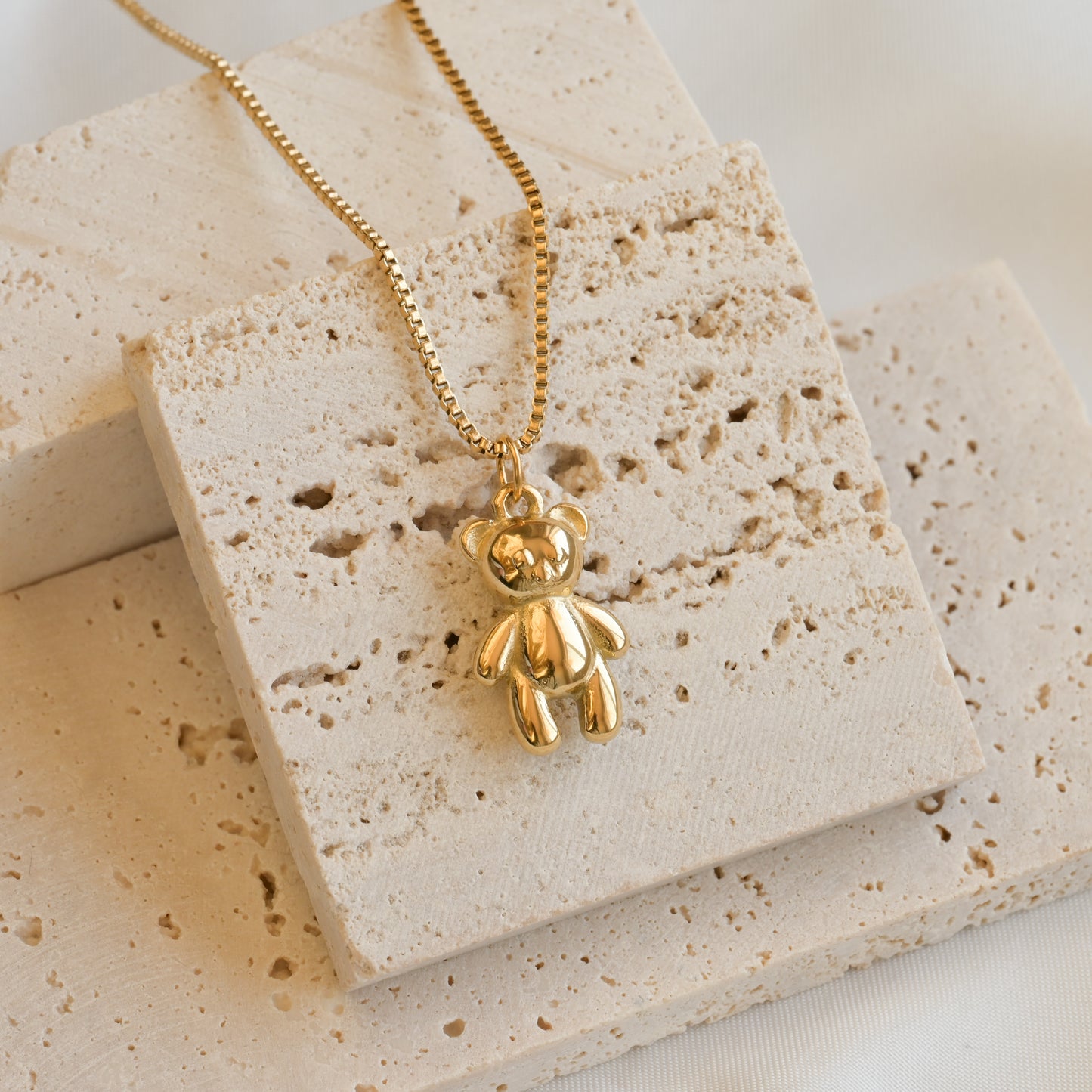 Gold bear necklace on a eige stone surface