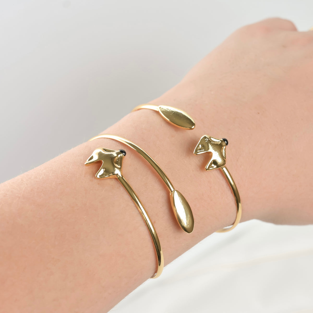 Close-up view of dainty gold fox bracelets with a wrap cuff design on a wrist against a light background