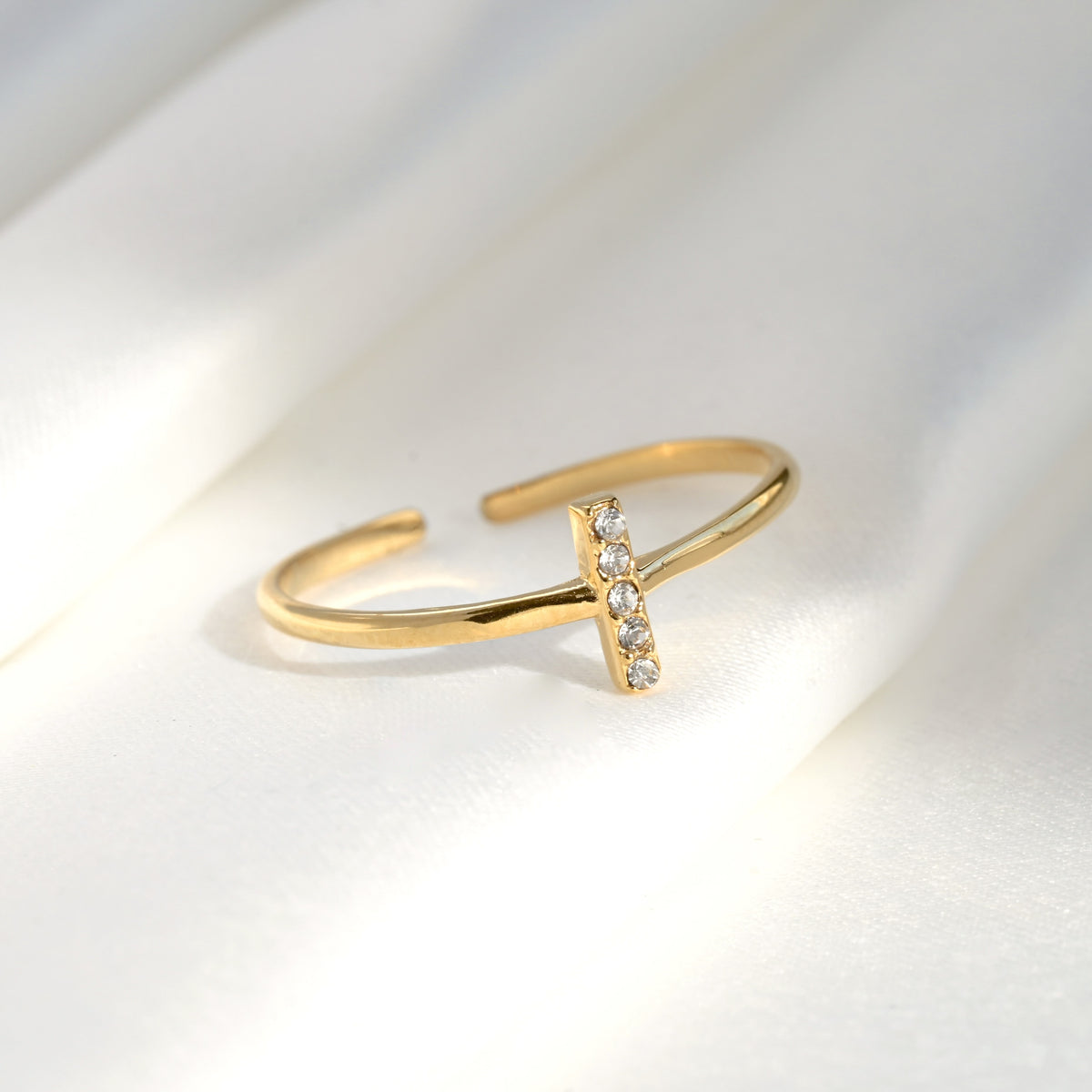 Open gold ring with a small diamond bar on a light gray background