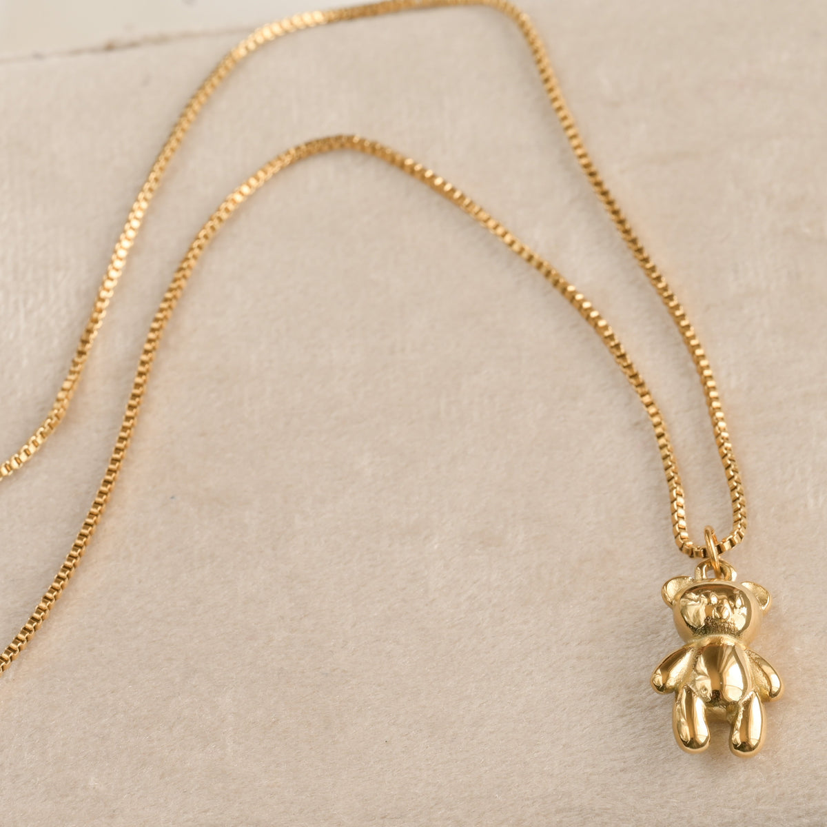 gold stuffie necklace with a box chain on beige surface
