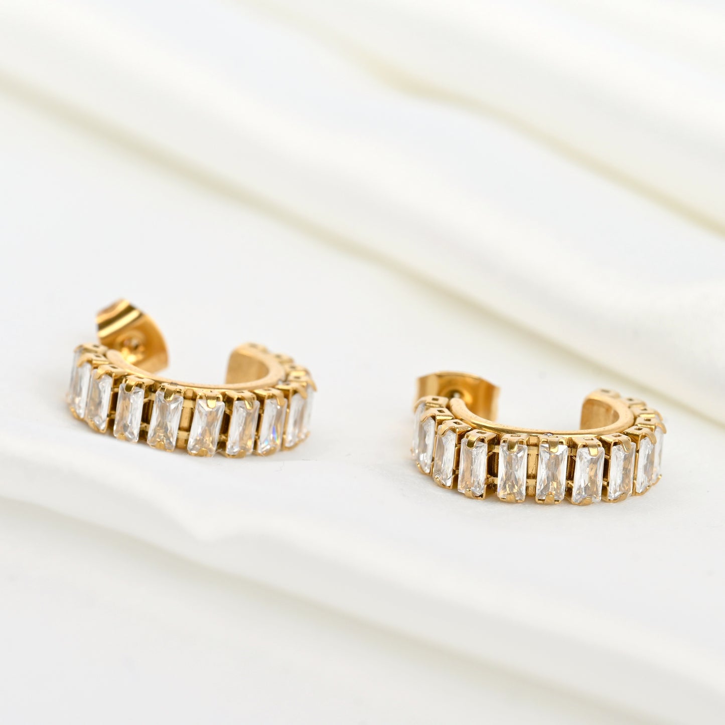 Gold hoop earrings with clear gemstones flat on a light background