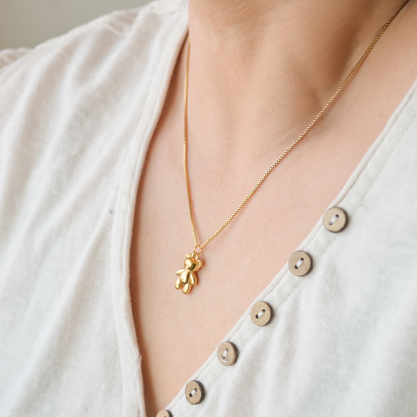Gold box chain with teddy bear charm on a persons neck