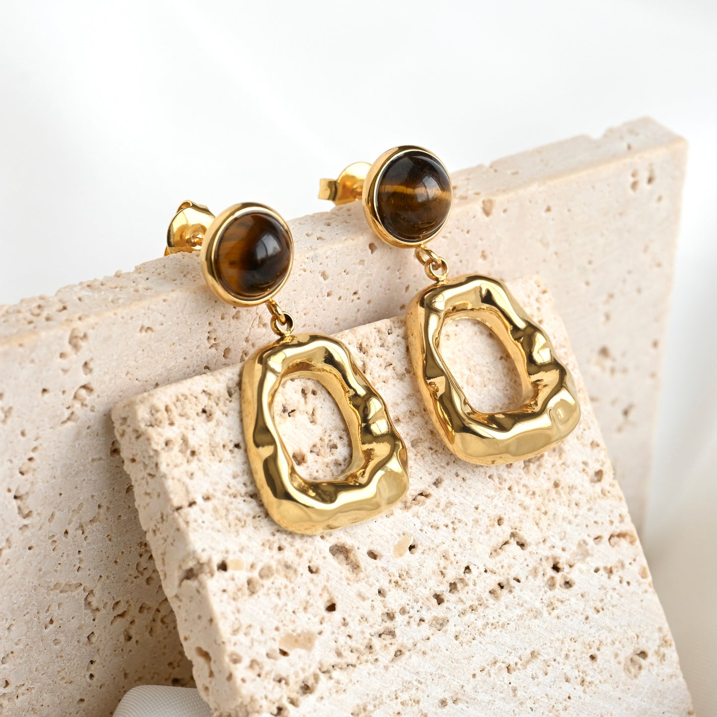 Gold earrings with tiger's eye stones on a textured stone surface