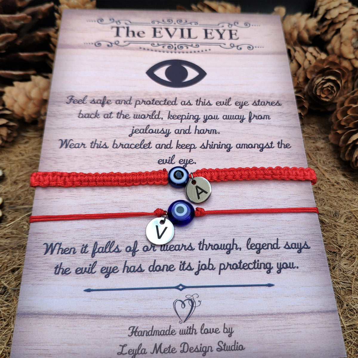 Two red bracelets with evil eye designs on a decorative card with text.