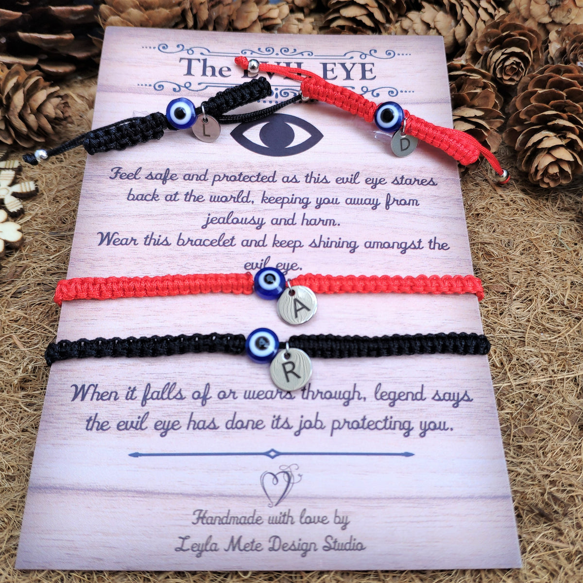 Two bracelets with evil eye charms on a decorative card with text, surrounded by pine cones and flowers.