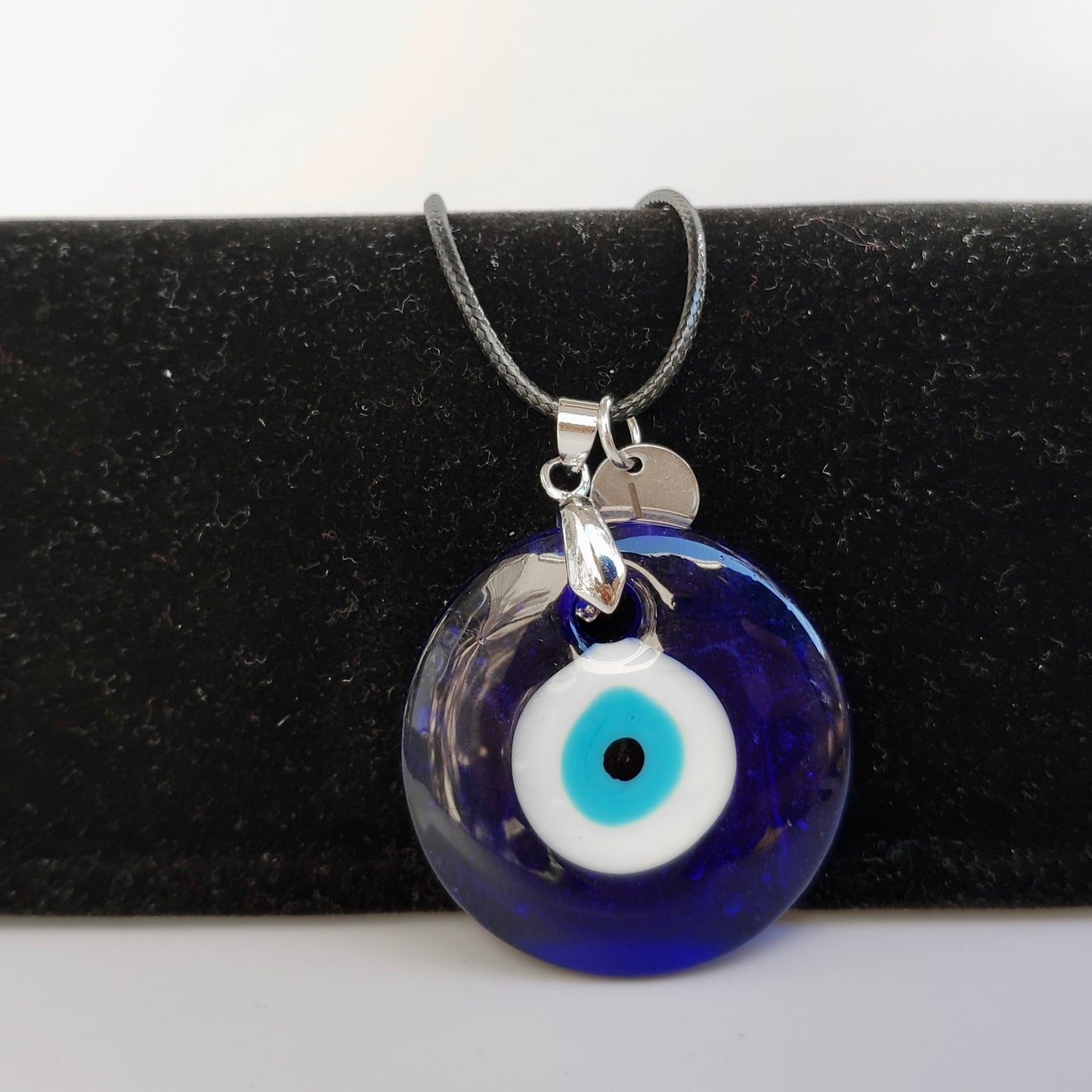 Blue evil eye pendant necklace on a black stand with a white background