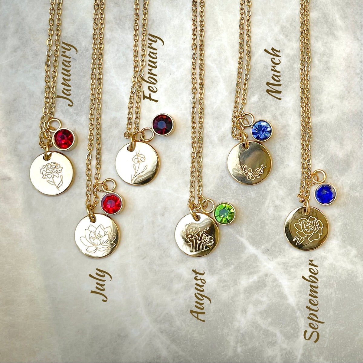 Gold flower necklaces with birthstone charms on a textured gray background
