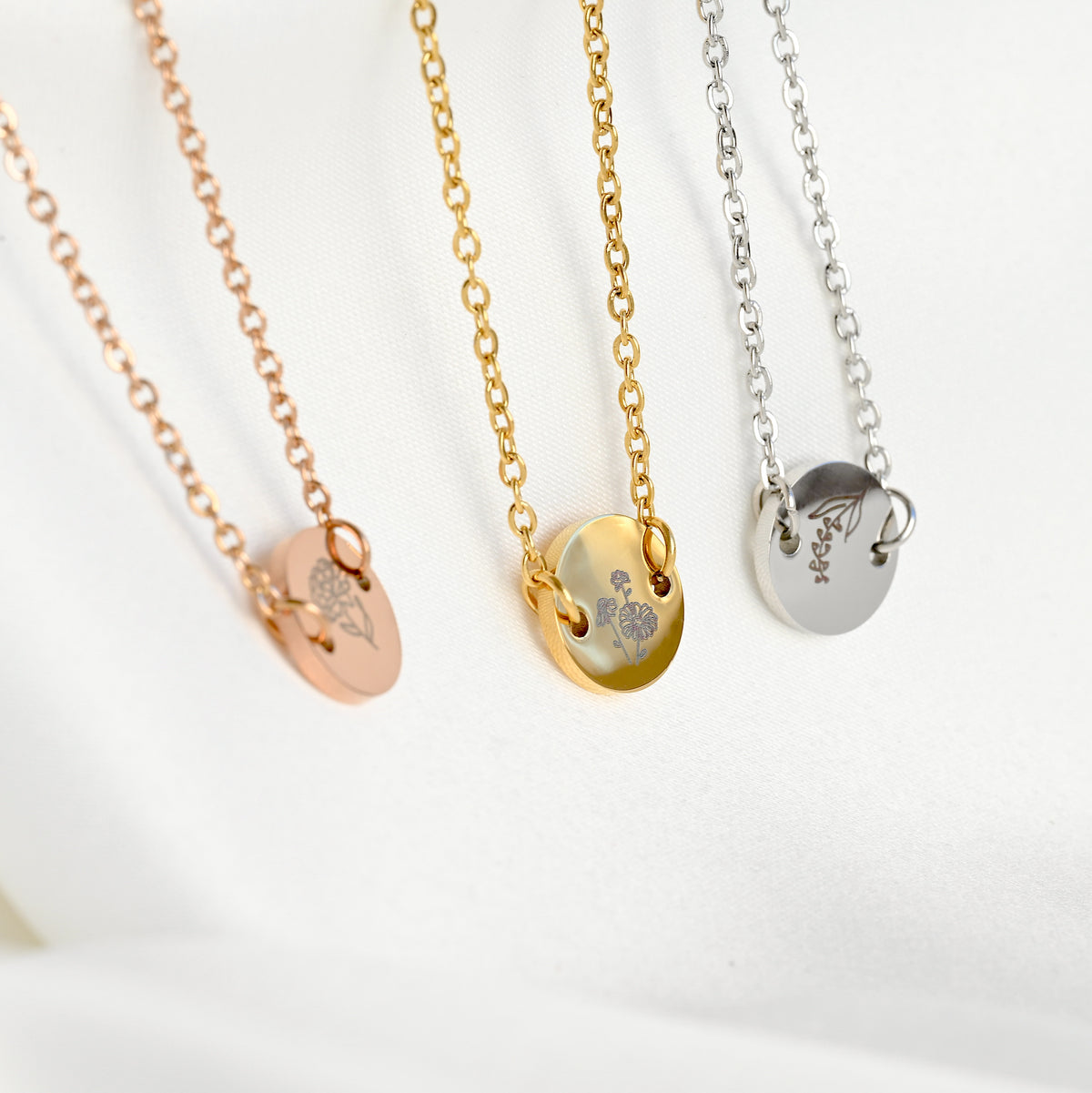 Side view of the rose gold, gold and silver bracelets with engraved birth flowers, showcasing the thickness of the coin charm on a white background
