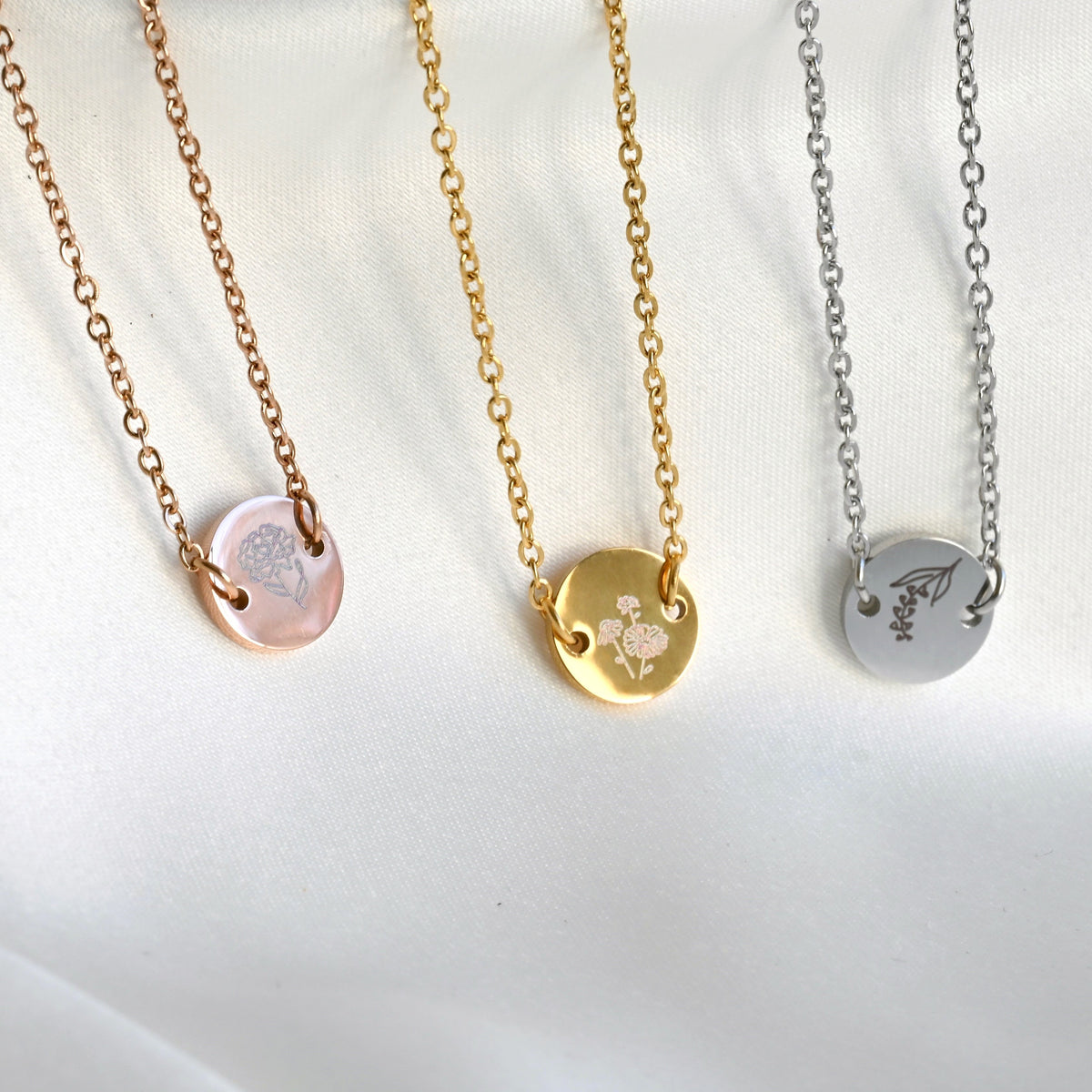 Three bracelet with circular flower pendants in rose gold, gold and silver from left to right, on a white background