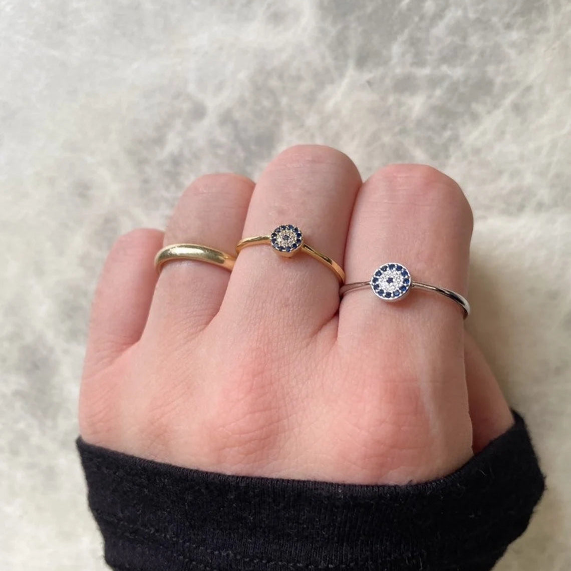 Top view of hand wearing two rings with gemstones on a neutral background
