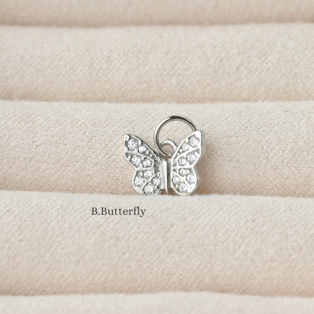 Butterfly-shaped silver charm with clear stones on a beige fabric background