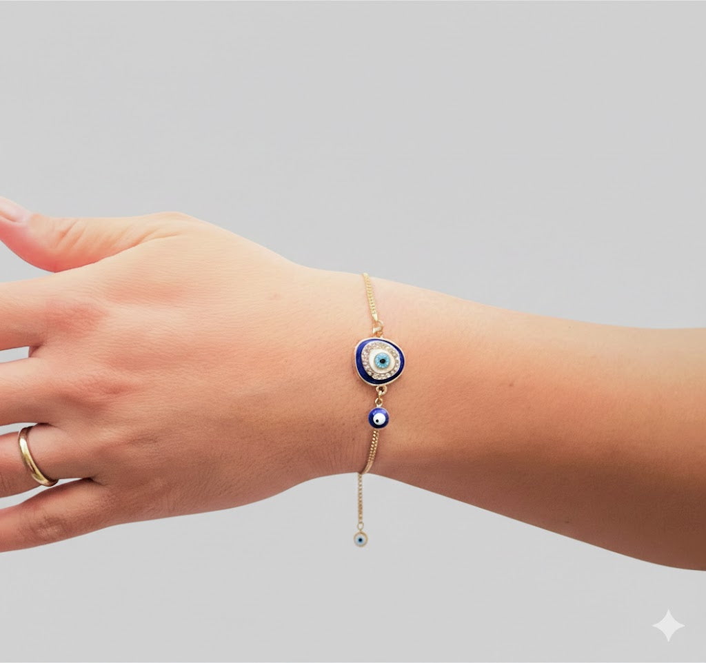 Hand wearing a gold bracelet with a colorful evil eye charm on a gray background