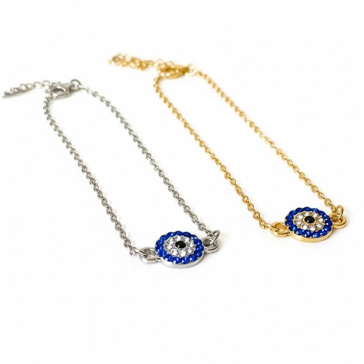 Two evil eye anklets with round crystal eye charms in silver and gold on a white background